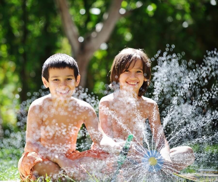 Two boys playing in the sprinkler in backyard