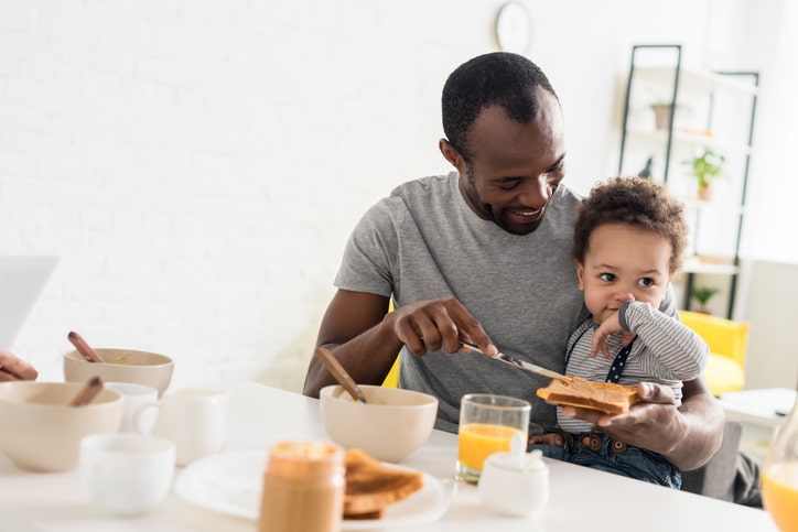Father applying peanut butter on toast for little son