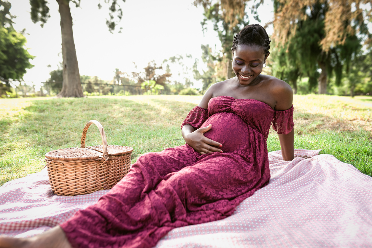 African woman caressing her pregnant belly while doing a picnic in park