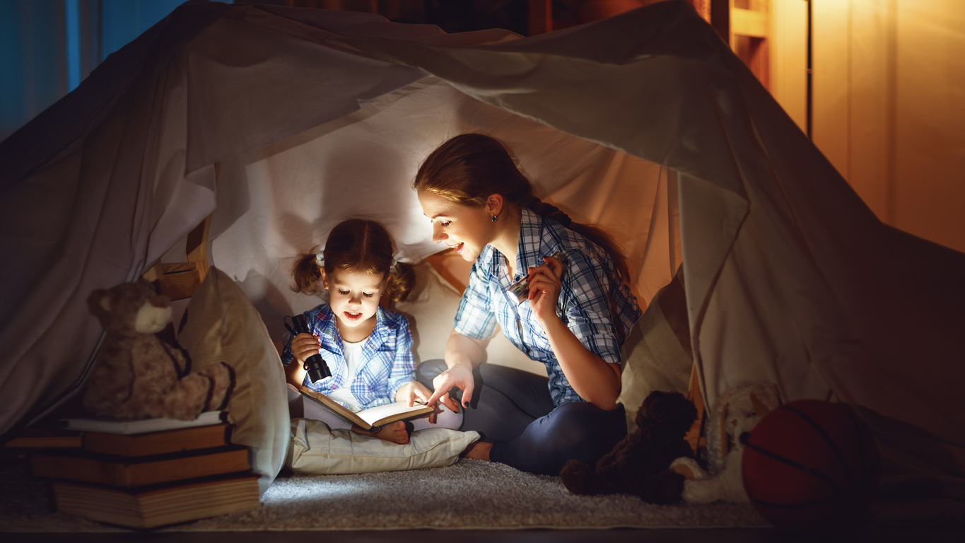 reading and family games in children's tent. mother and child daughter with book and flashlight before going to bed