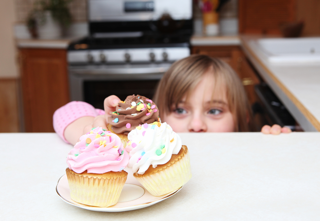 Little girl peeking over the counter while sneaking a cup cake
