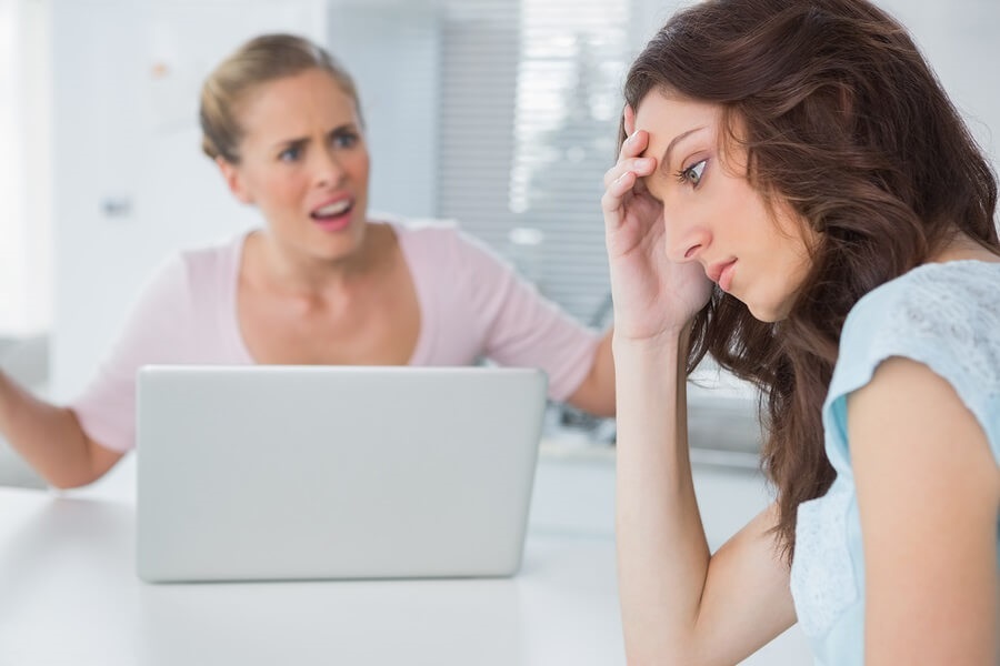 Two annoyed women sitting at a table on the computer