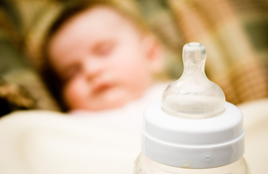 Close up of baby bottle with baby sleeping in background
