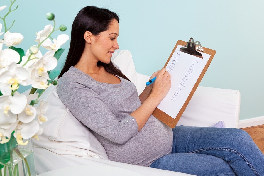 Pregnant woman sitting on couch making baby name checklist