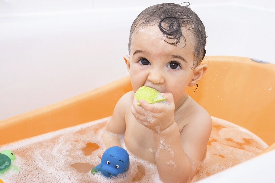 Young Child taking a bath and putting bath toy in mouth