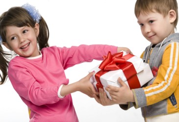 Young boy giving Valentine's Day gift to girl against white back drop
