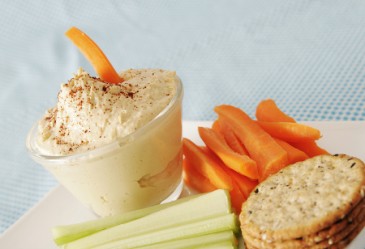 Carrots, celery, and crackers on plate with bowl od hummus.