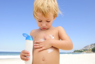 Young boy putting on sunscreen at the beach