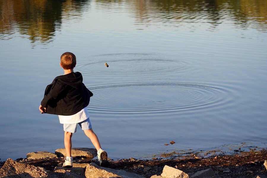 Summer Science for Kids, Child tossing rocks on a pond to learn physics of waves