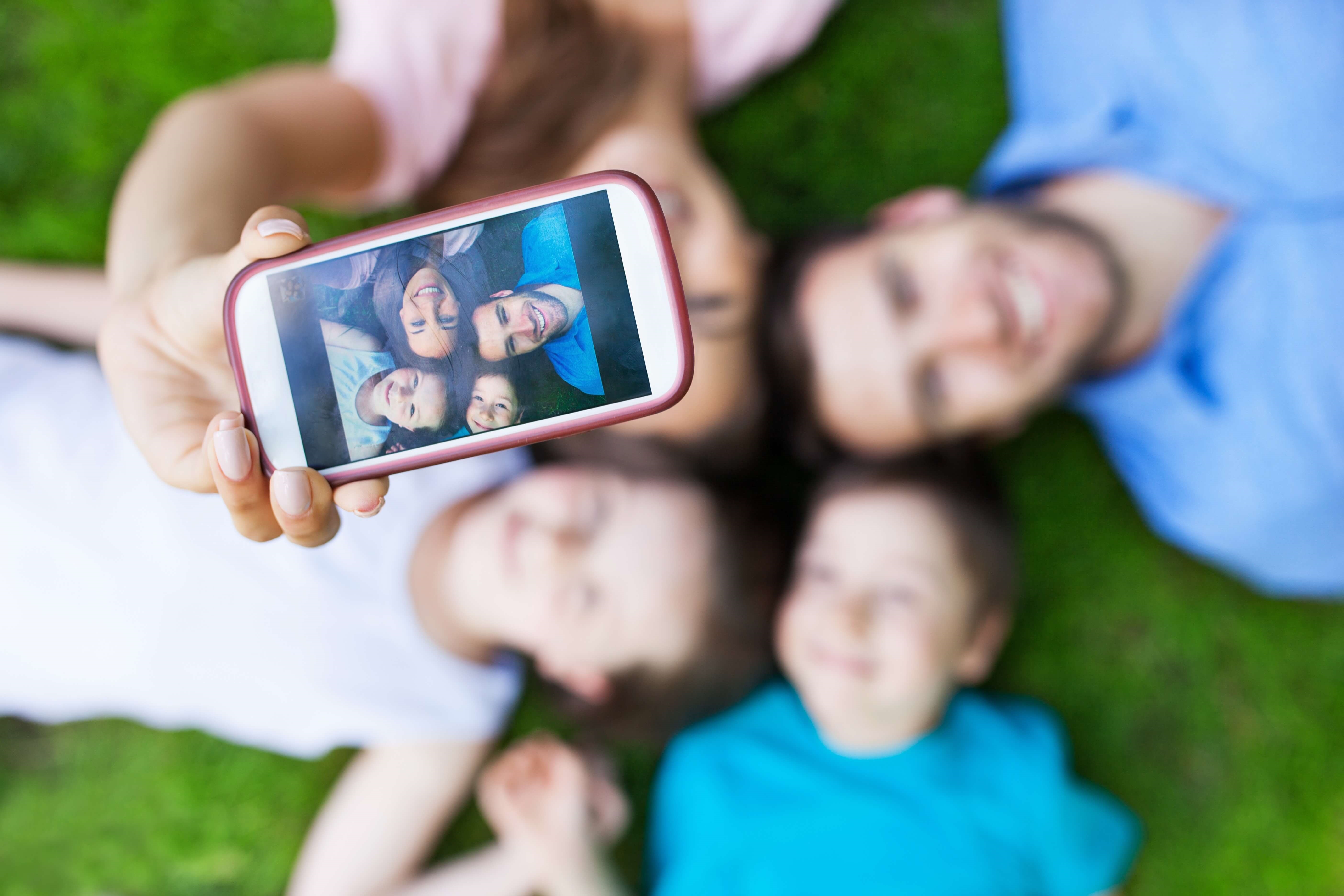 Family laying on lawn taking family selfie with smartphone