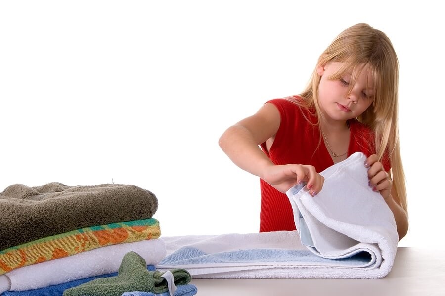 Young girl folding towels against white back drop.