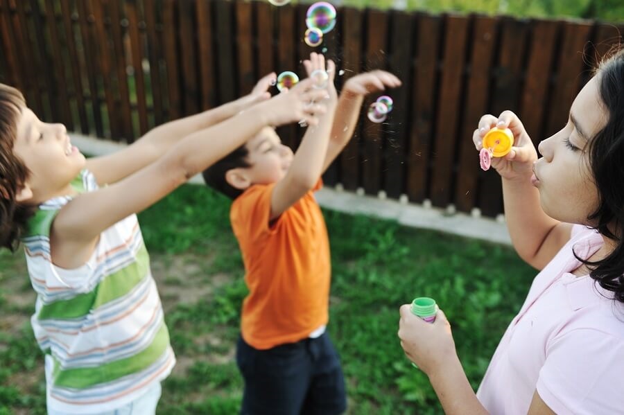Happy kids blowing bubbles and playing in backyard