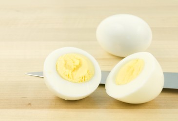 Hard-boiled egg cut in half, with knife and whole egg in background.