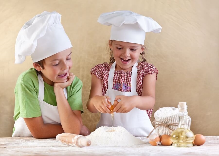 Two kids in aprons cracking eggs and baking
