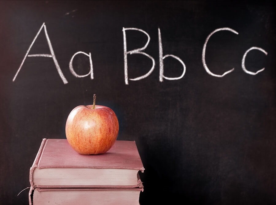 Apple on top of books with alphabet on chalkboard in background.