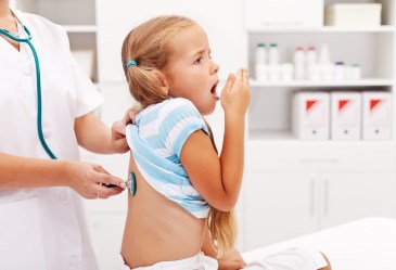 Little girl coughing and getting examined by doctor