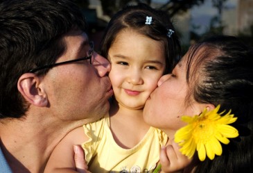Close up of two parents kissing happy child's cheeks.