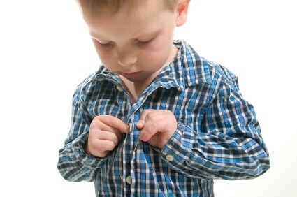 Young boy buttoning shirt and getting dressed against white background