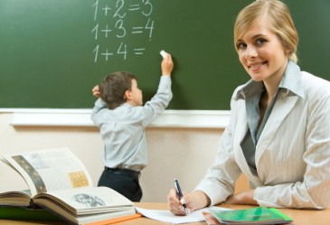 Close up of teacher with child writing on chalkboard in background