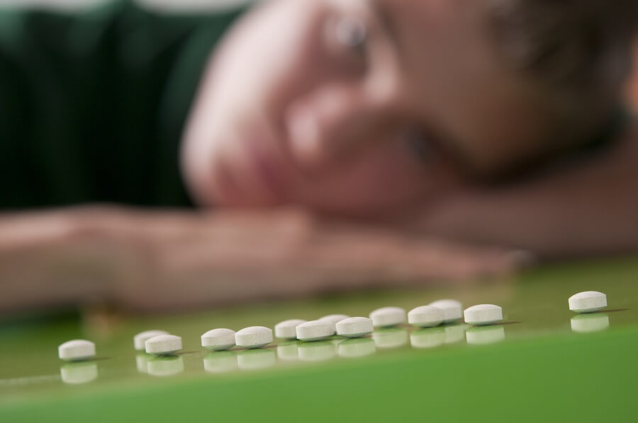 Row of white pills with teen arm in background