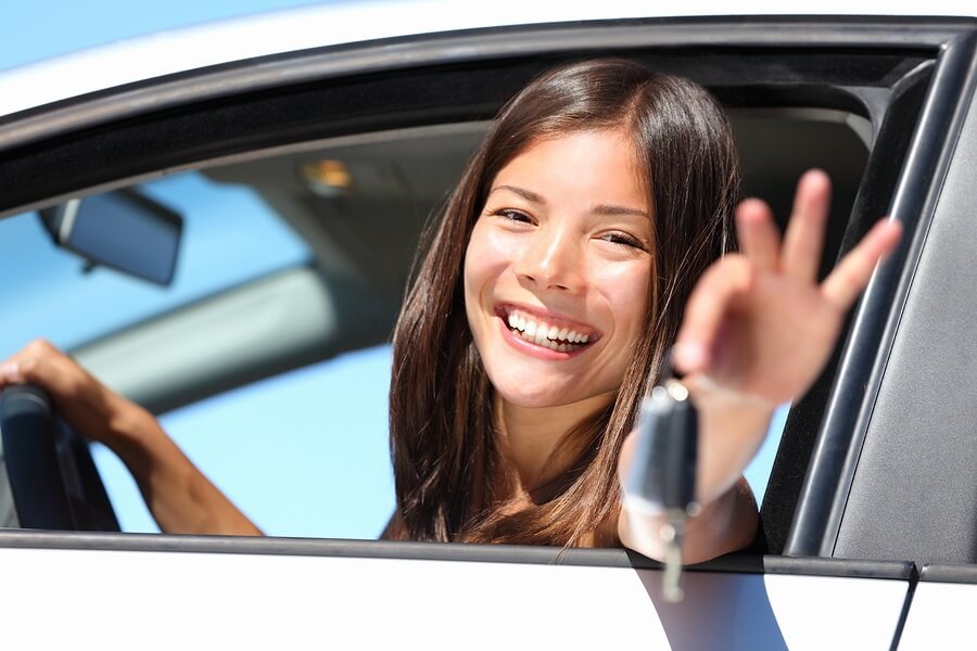 Smiling teen girl holding car keys out window