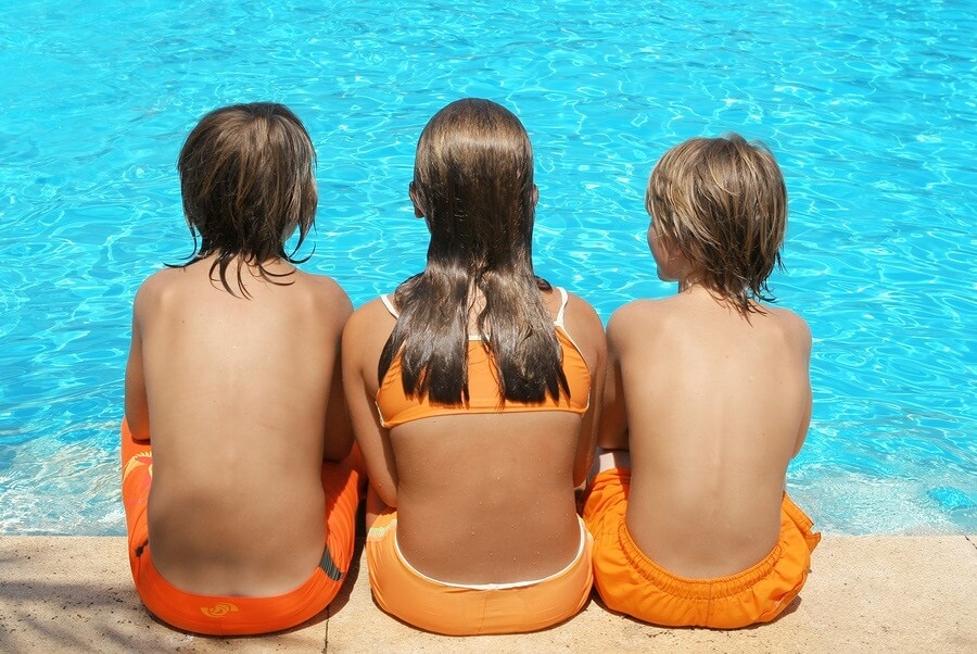 Three kids sitting on the side of a pool