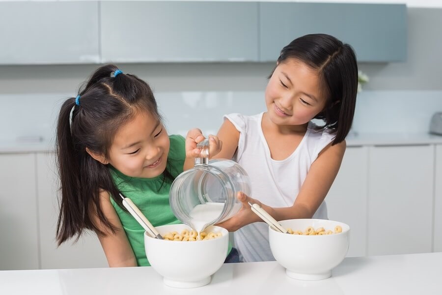 Two young girls pouring milk on cereal in kitchen