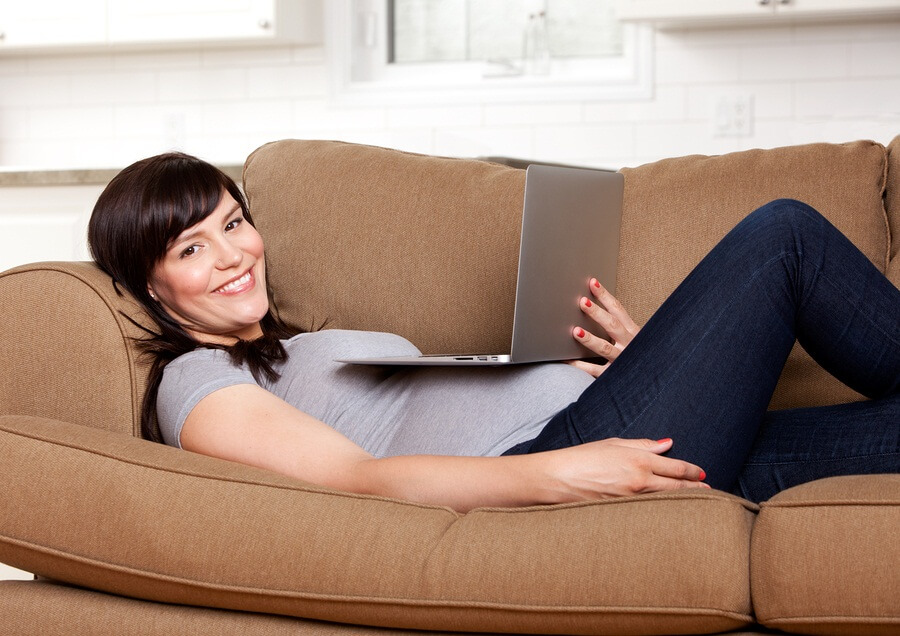Pregnant woman laying on couch watching movie on computer