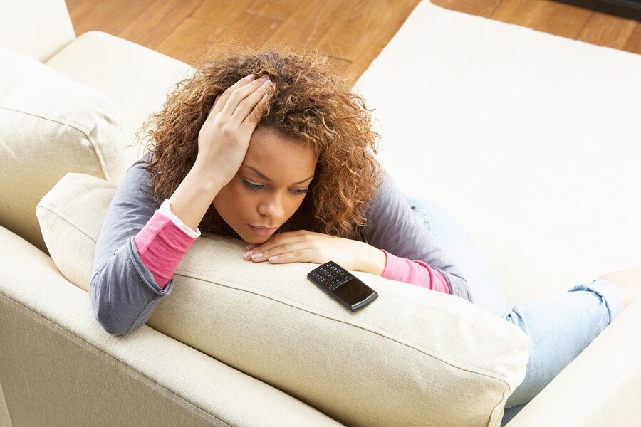 Sad woman sitting on couch looking at phone