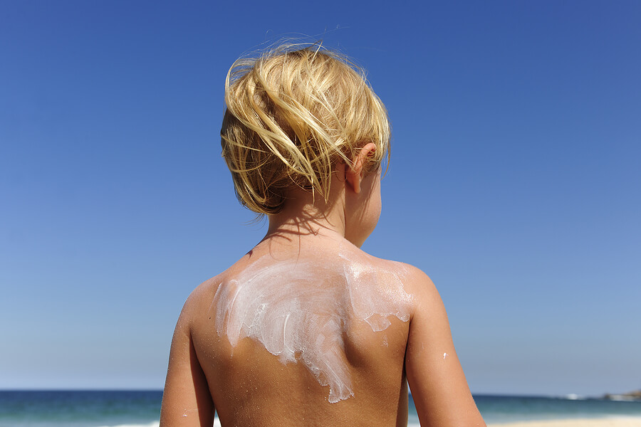 Summer camp essentials, young boy child with sunscreen on back at beach