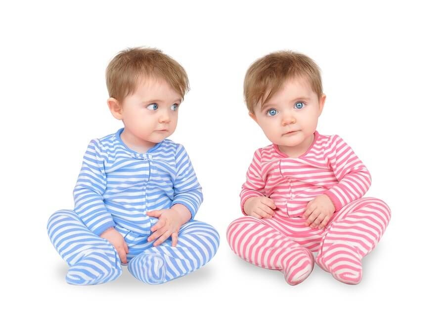 Twins in striped pink and blue pajamas against white background
