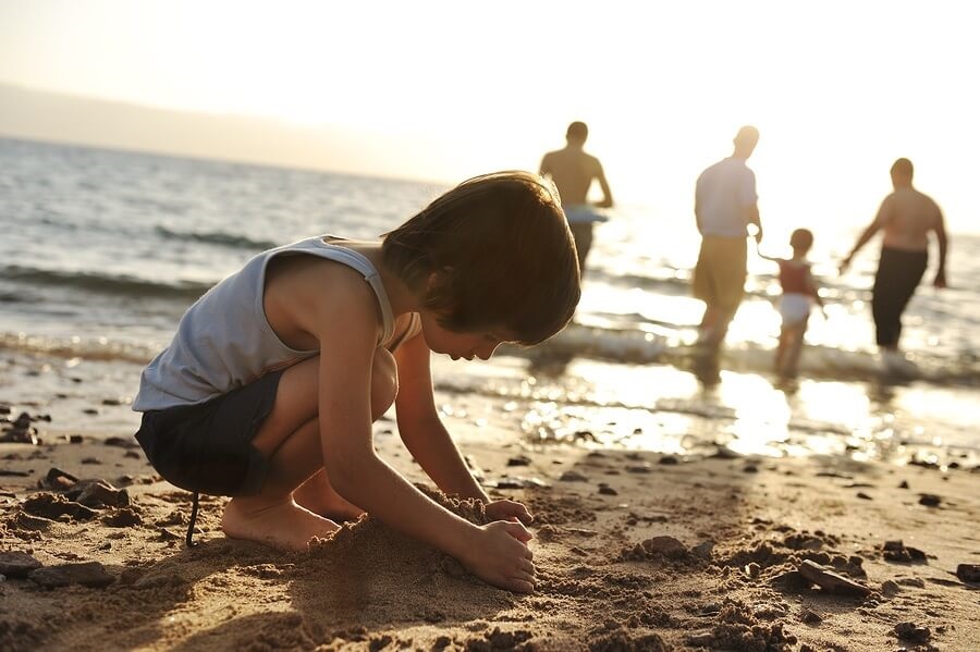 Child playing in the sand with family in the background