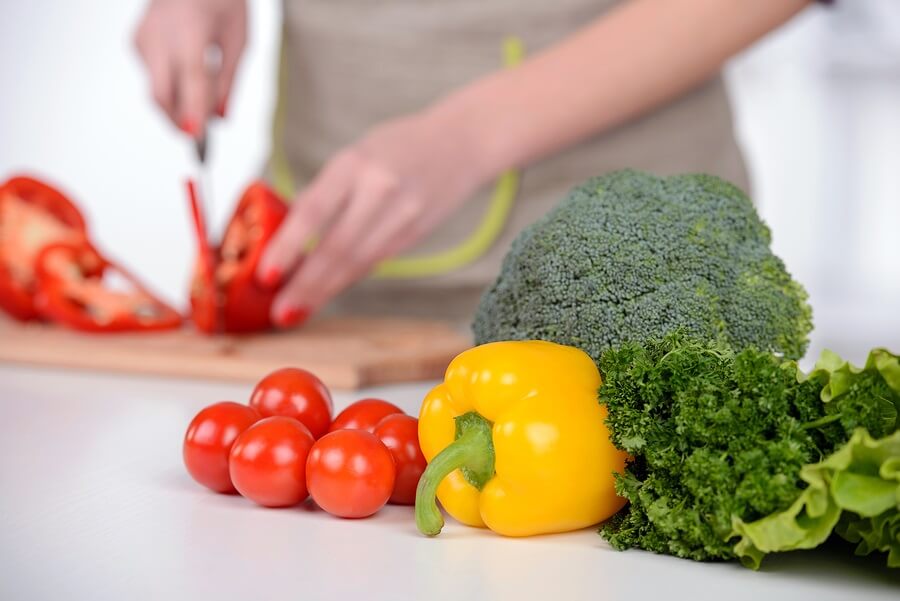 Pile of vegetables with woman cutting vegetables in background