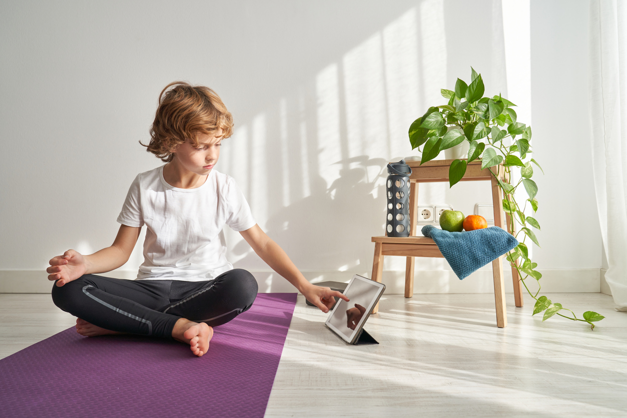 Full body of focused preteen boy browsing tablet while preparing for online yoga lesson at home