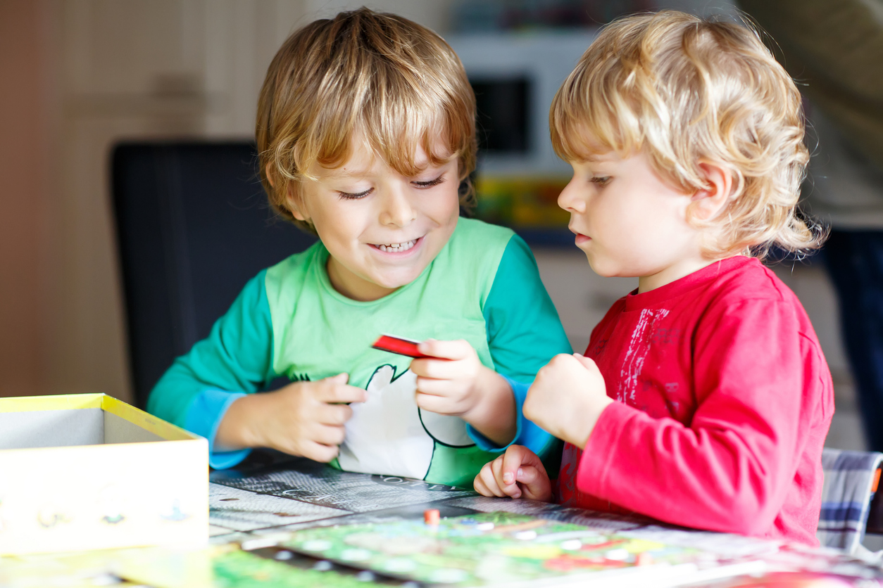 Two little blond kid boys playing together board game at home. Funny siblings having fun.