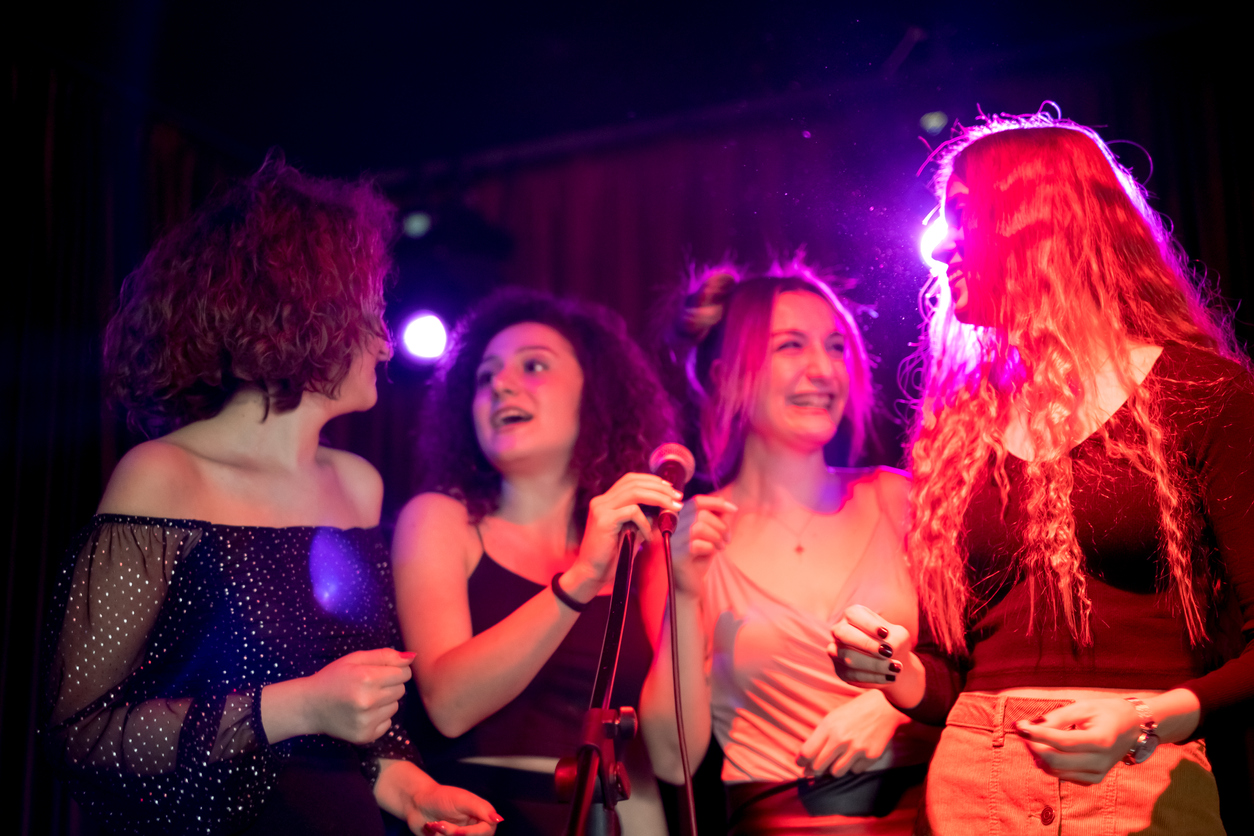 Girls are smiling dancing singing and enjoying the night at karaoke party