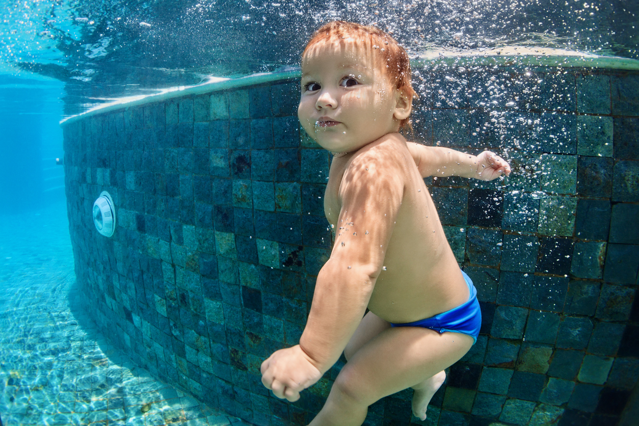 Funny photo of active baby swimming and diving in pool with fun - jump deep down underwater with splashes and foam. Family lifestyle and summer children water sports activity and lessons with parents.