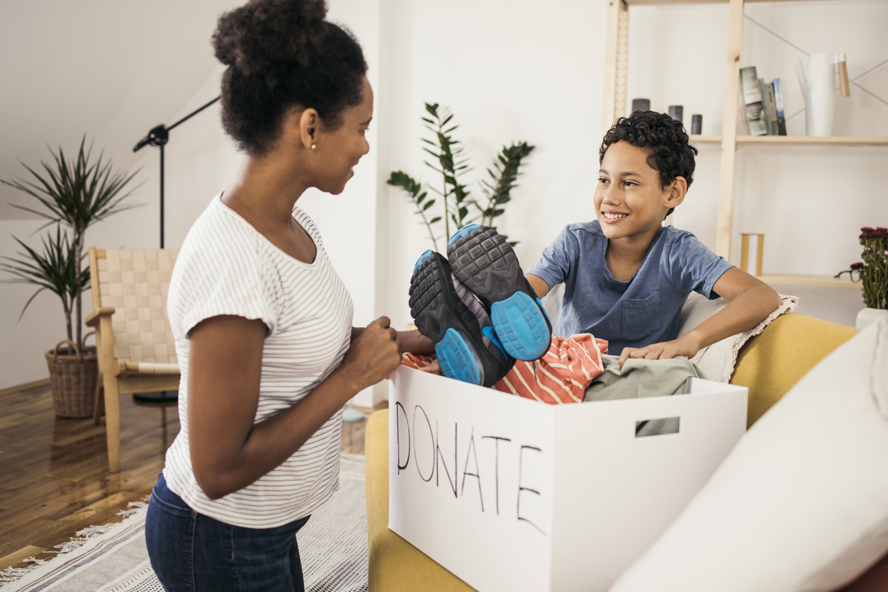 Mother and young child packing old clothes into a cardboard box that says "Donate"