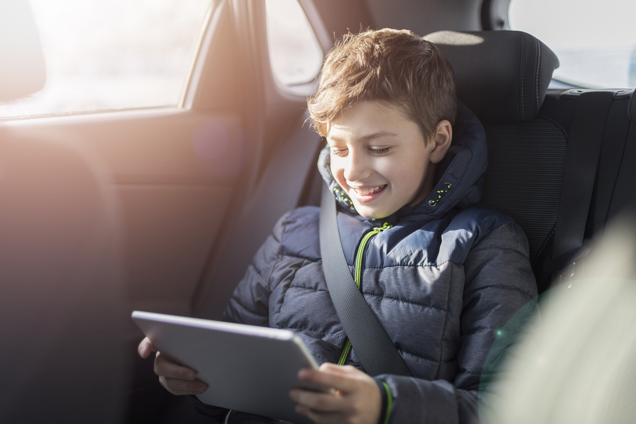 Teenage boy using digital tablet in the back seat of car. Safety of transportation of children