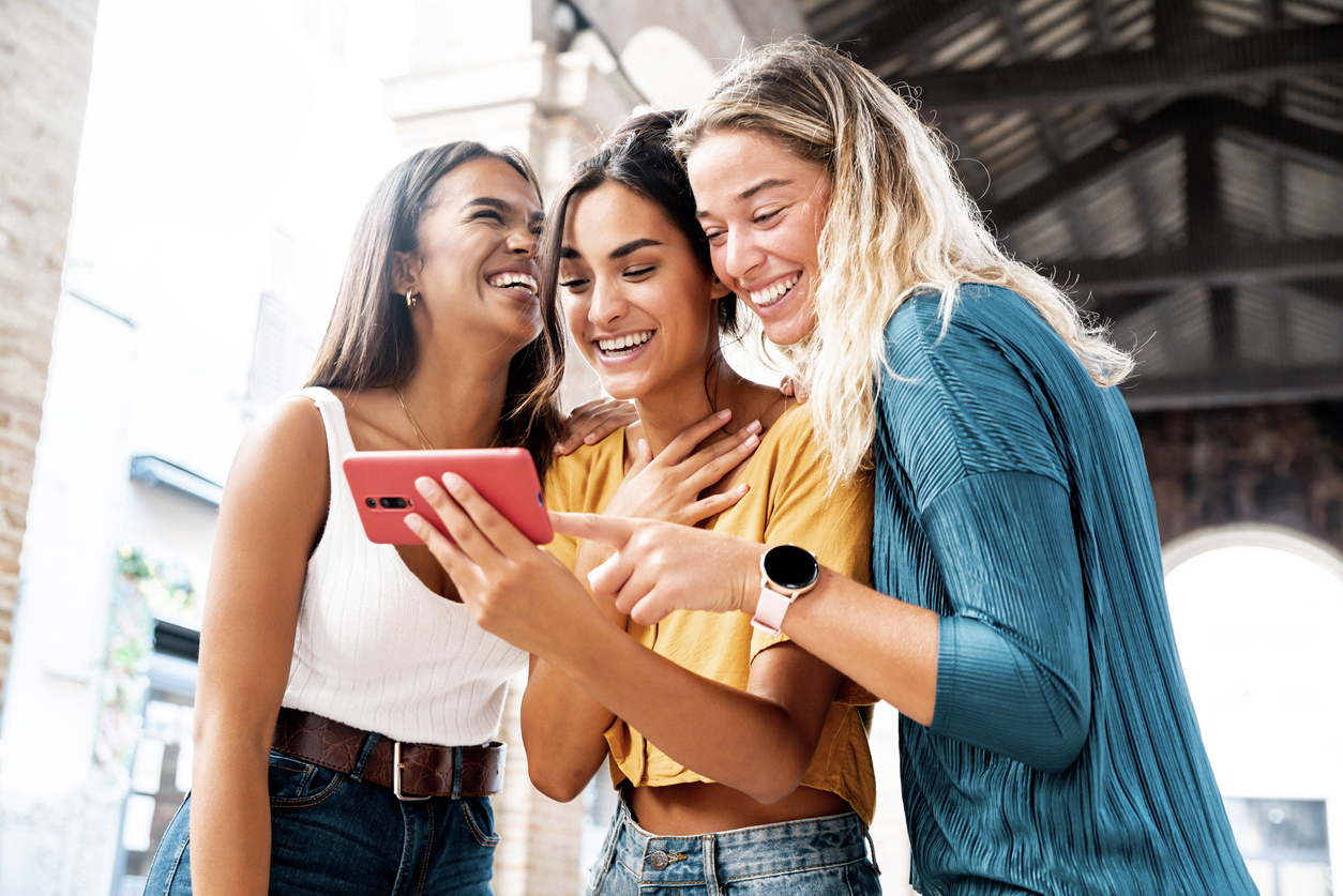 Three happy friends watching a smart phone mobile outdoors - Gen Z women using cellphone on city street - Technology, social, friendship and youth concept