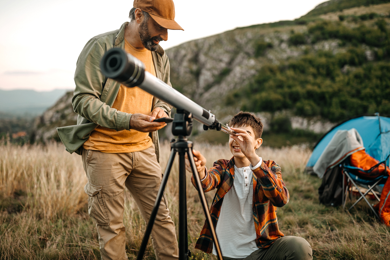 Father and son adjusting telescope on a camp site