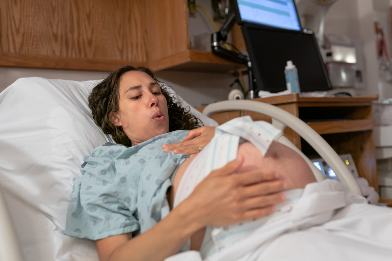Woman is in the throes of childbirth. She is breathing heavily but looks confident and prepared for what is to come.