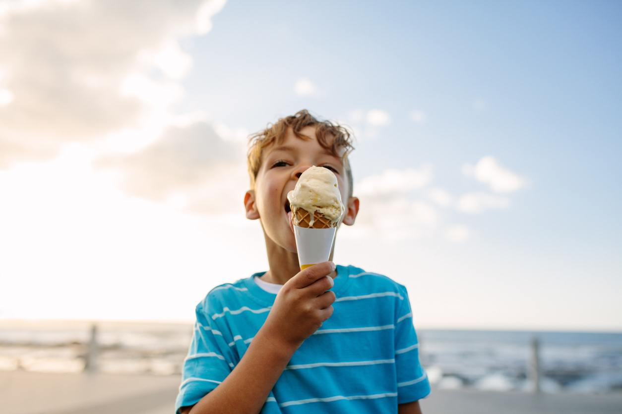 Boy eating an ice cream standing near seafront. Little boy on vacation treating himself to an ice cream.