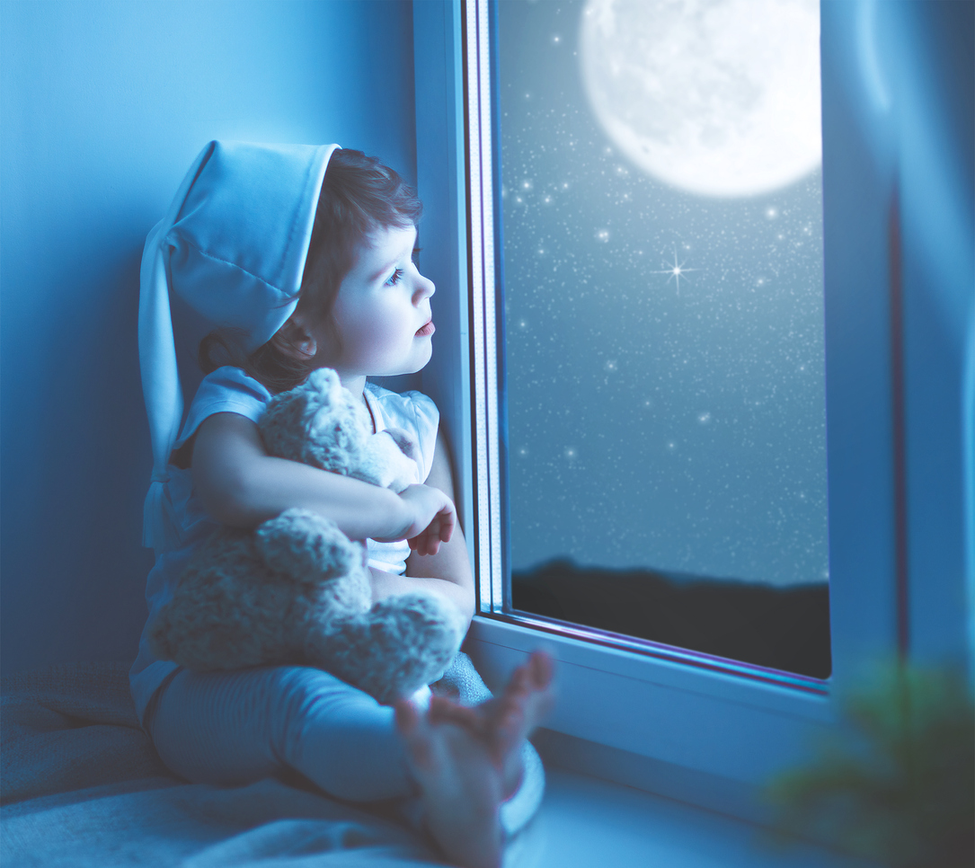 Little boy looks out the window at the moon. Night time.