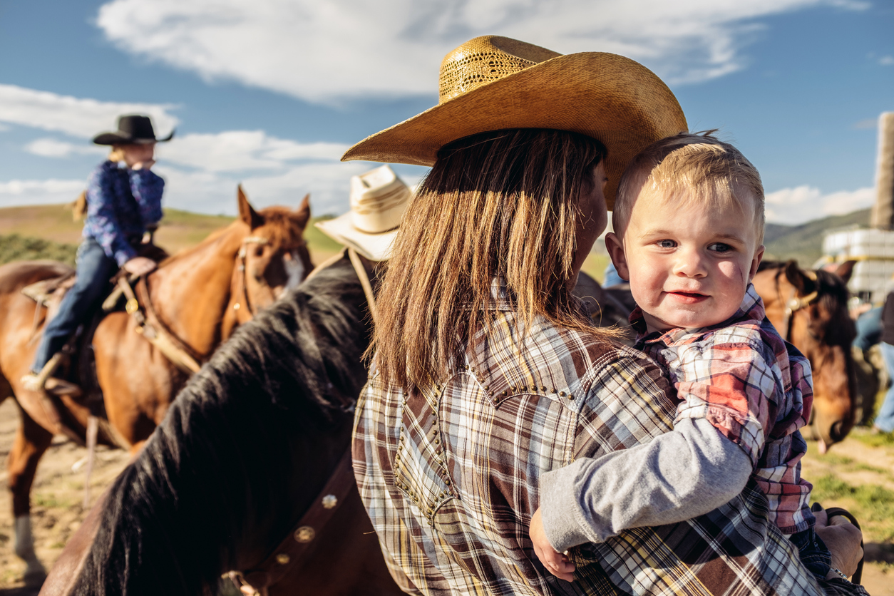 Portrait of young cowgirl mother and baby outdoors. Horse in the background. Outside Salt Lake City, Utah.