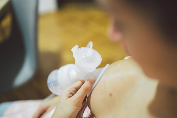 Unrecognizable woman using a breast pump, pumping out milk for baby, high angle view