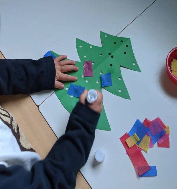 Child gluing tissue paper to paper Christmas tree craft 