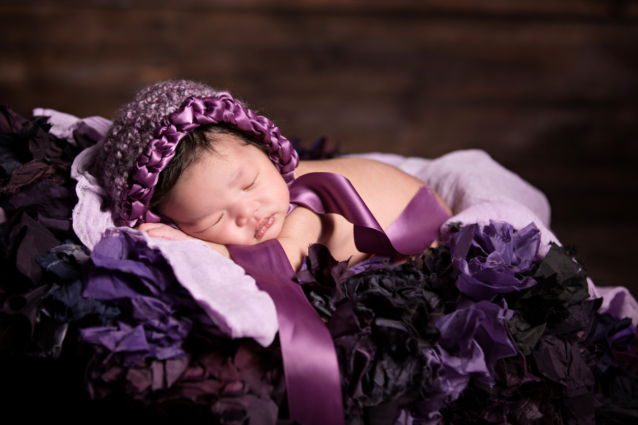 Asian baby dressed in purple sleeps on purple blanket