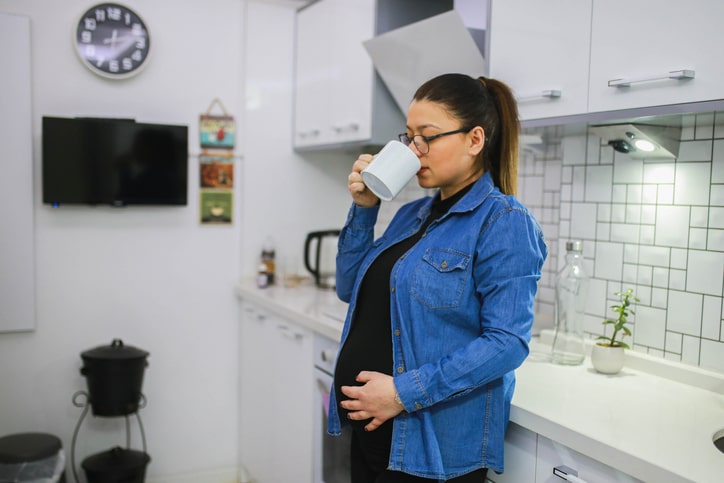 Pregnant young woman drinking coffee in the kitchen
