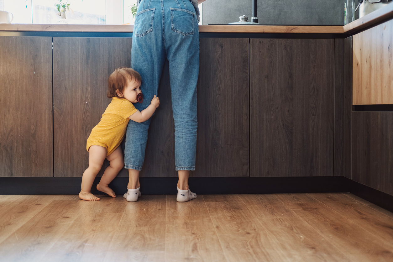 Baby girl standing by mother's legs at home in kitchen